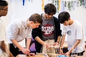 Four young adults looking at a bamboo model they are making from skewers.